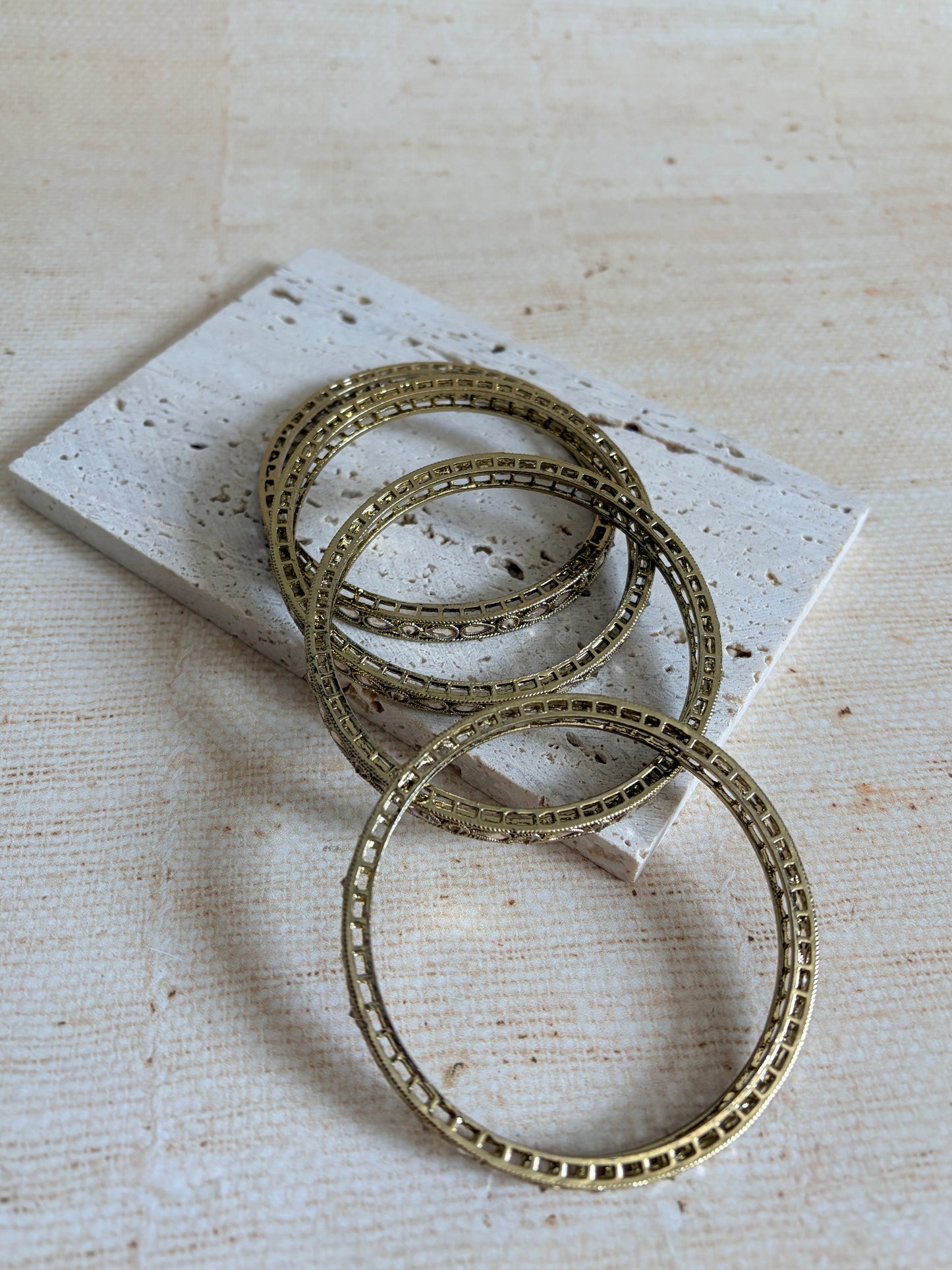 Three gold bangles on a textured beige surface