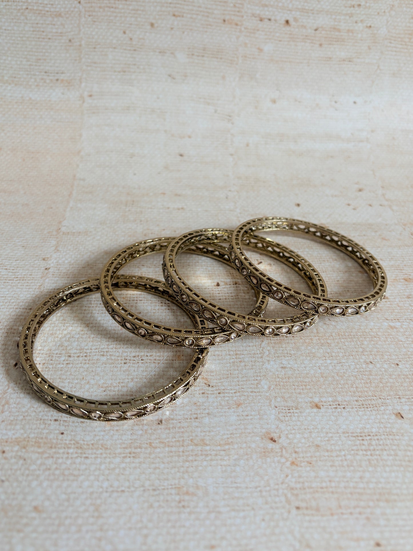Set of four ornate gold rings on a textured beige background