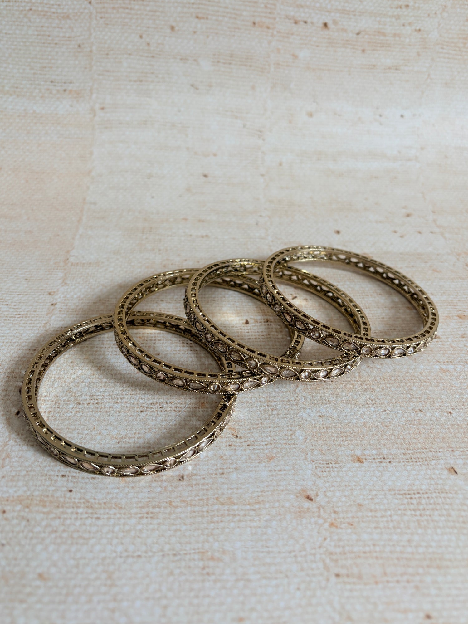 Set of four ornate gold rings on a textured beige background
