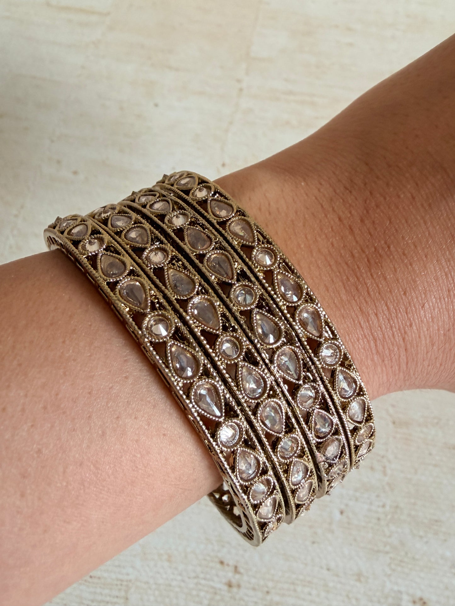 Close-up of a person's wrist wearing a decorative gold bracelet with gemstones on a light background.