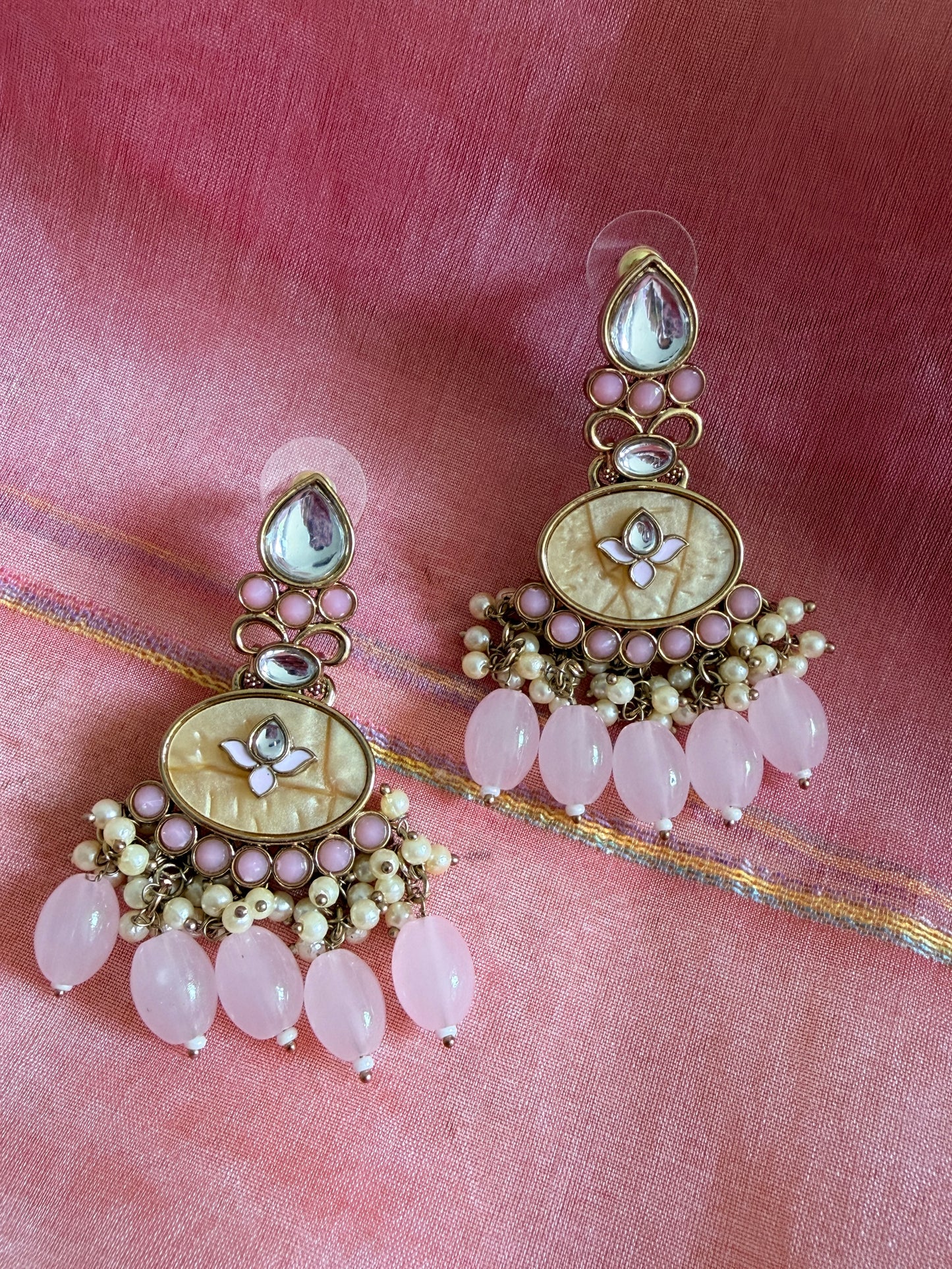 Ornate earrings with pink stones on a pink fabric background