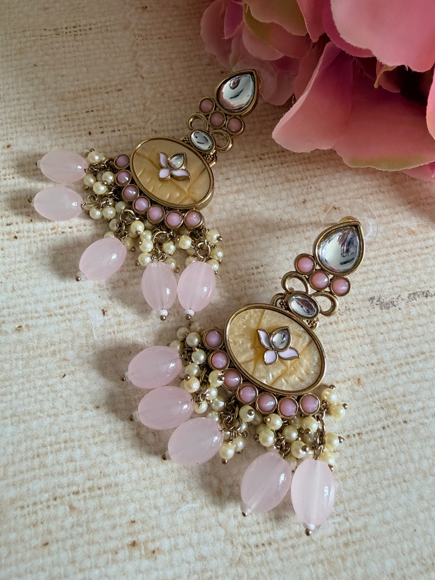 Ornate necklace with pink beads and floral elements on a textured surface with flowers.