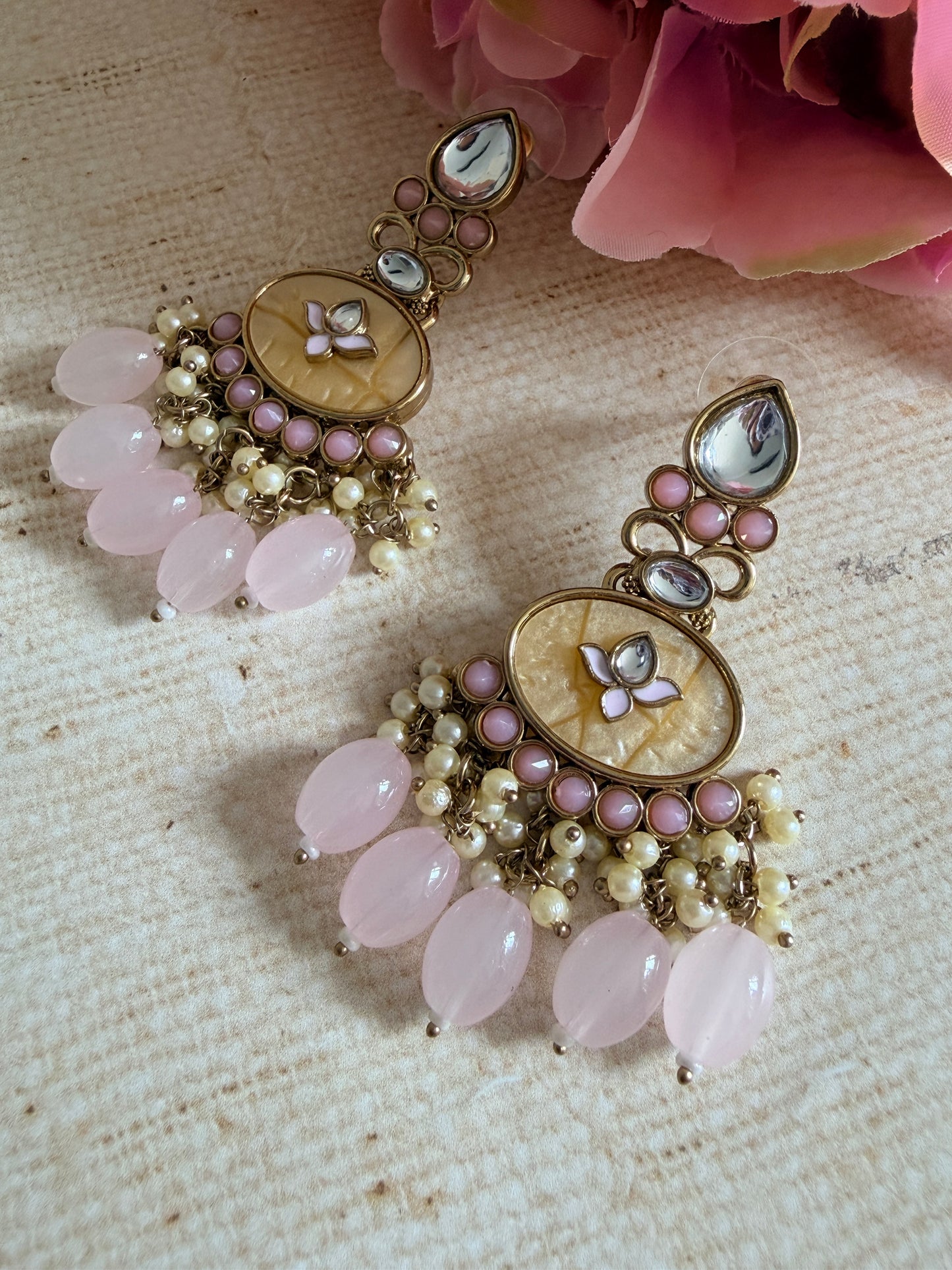 Ornate earrings with pink stones and floral designs on a textured surface.