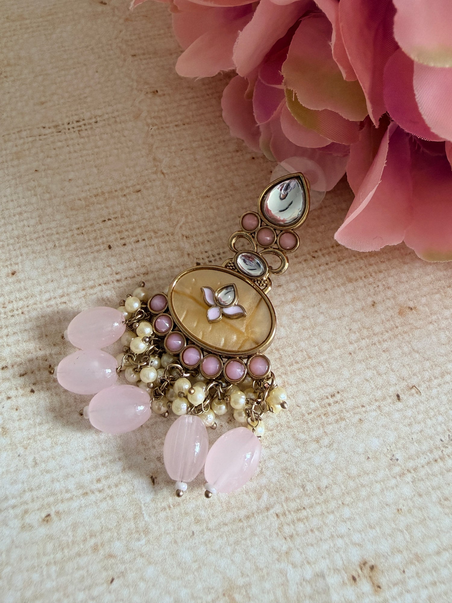 Decorative brooch with pink stones and pearl-like beads on a textured beige background with pink flowers.