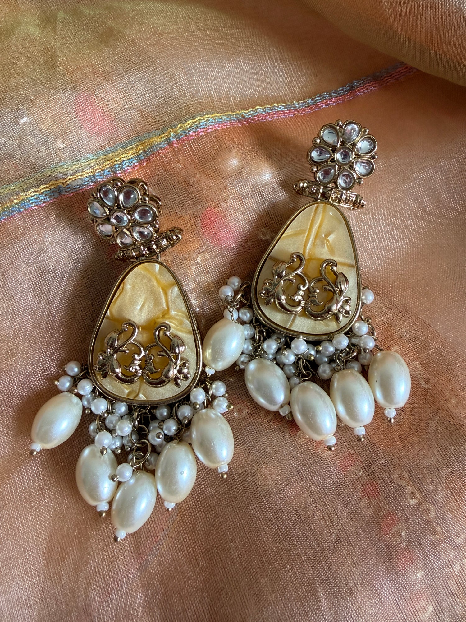 Pair of ornate earrings with pearl-like stones on a fabric background