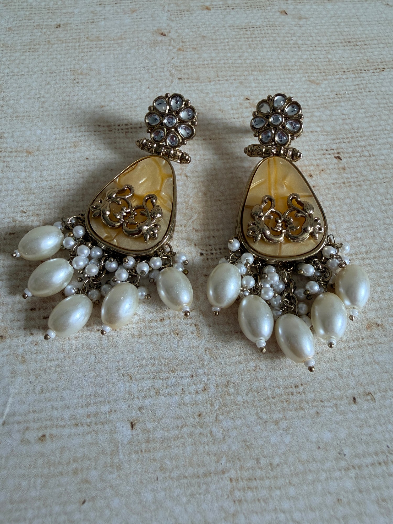 Pair of pearl and crystal earrings on a textured beige background