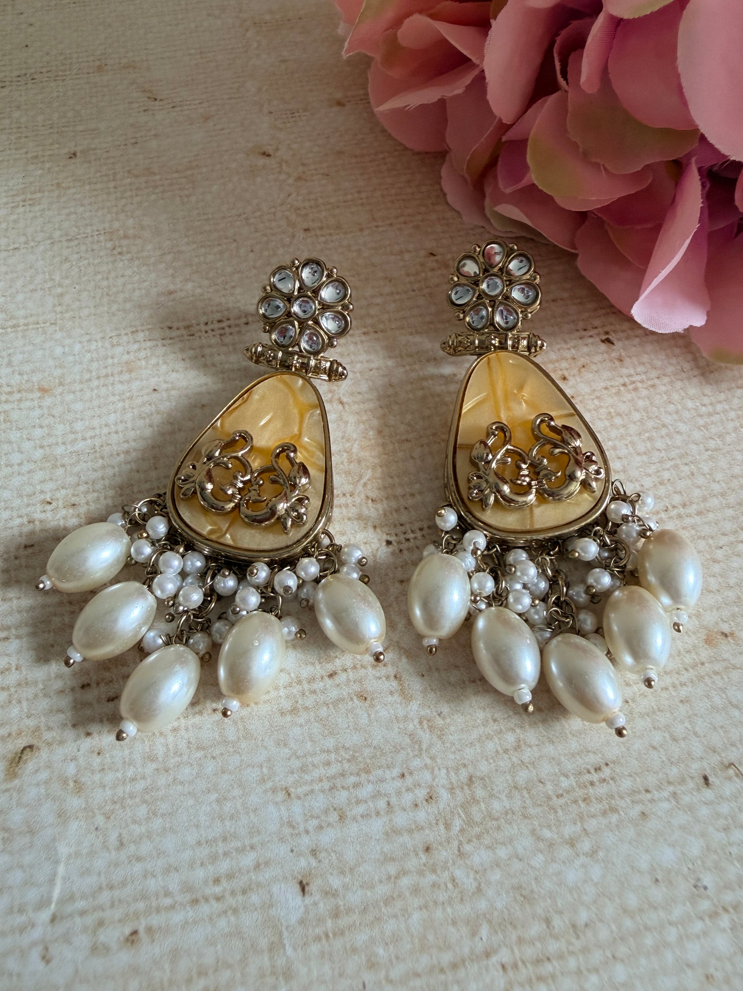 Pair of gold and pearl earrings on a textured surface with pink flowers.