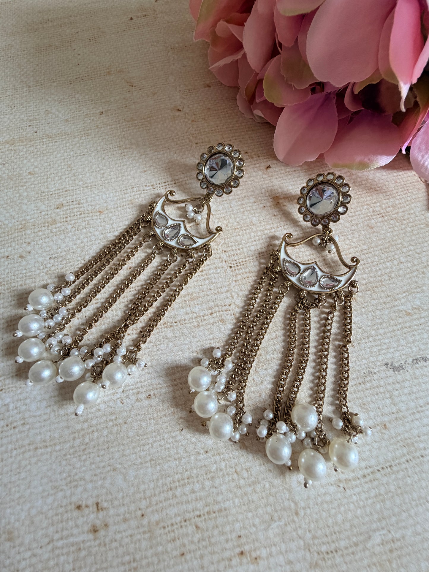 Pair of vintage-style earrings with pearl-like beads on a textured fabric background.
