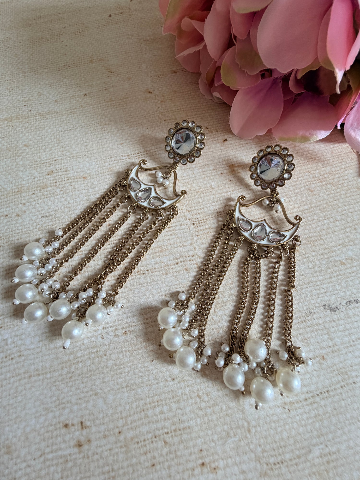 Pair of vintage-style earrings with pearl-like beads on a textured fabric background.