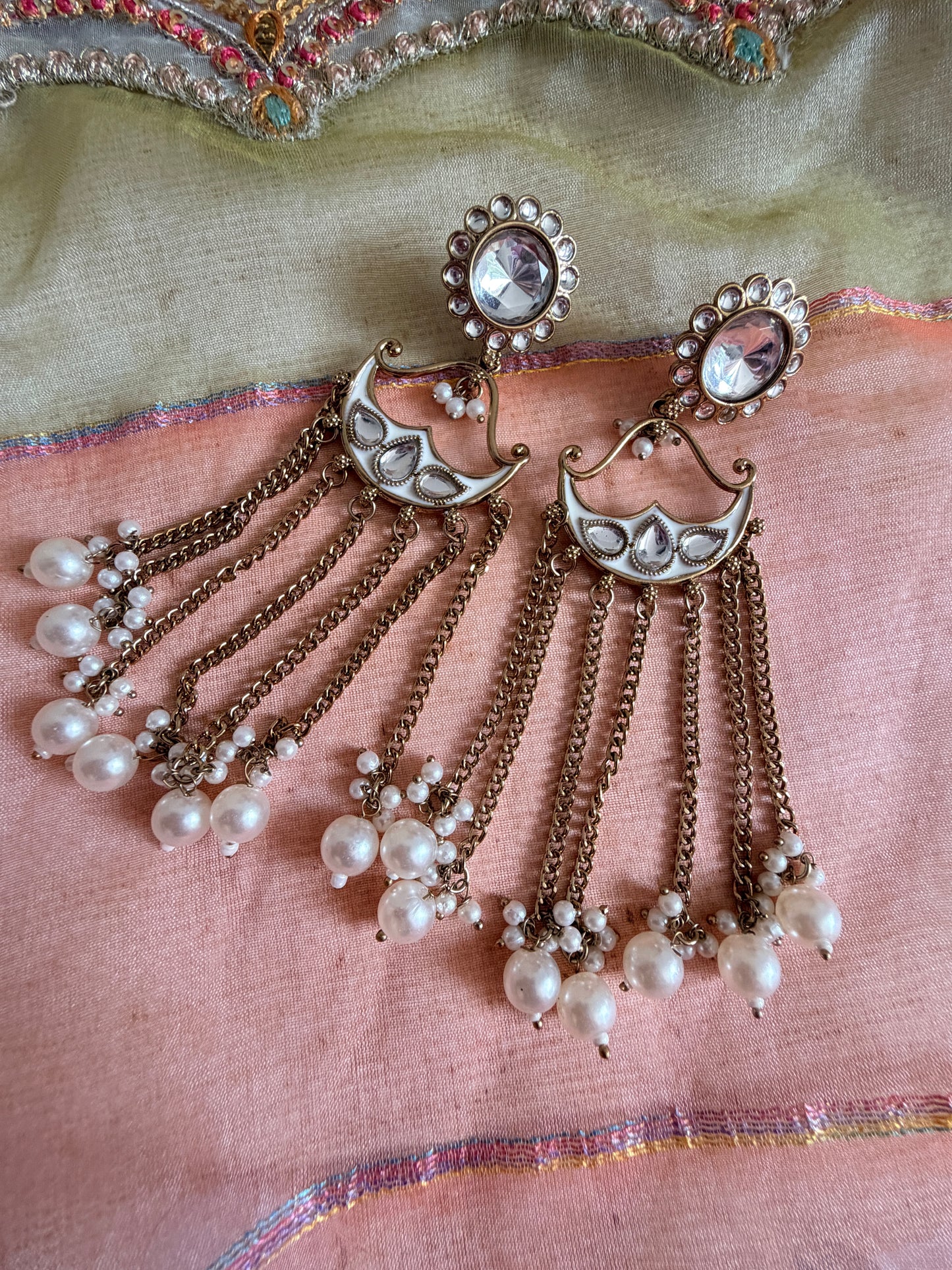 Decorative earrings with chains and pearls on a fabric background