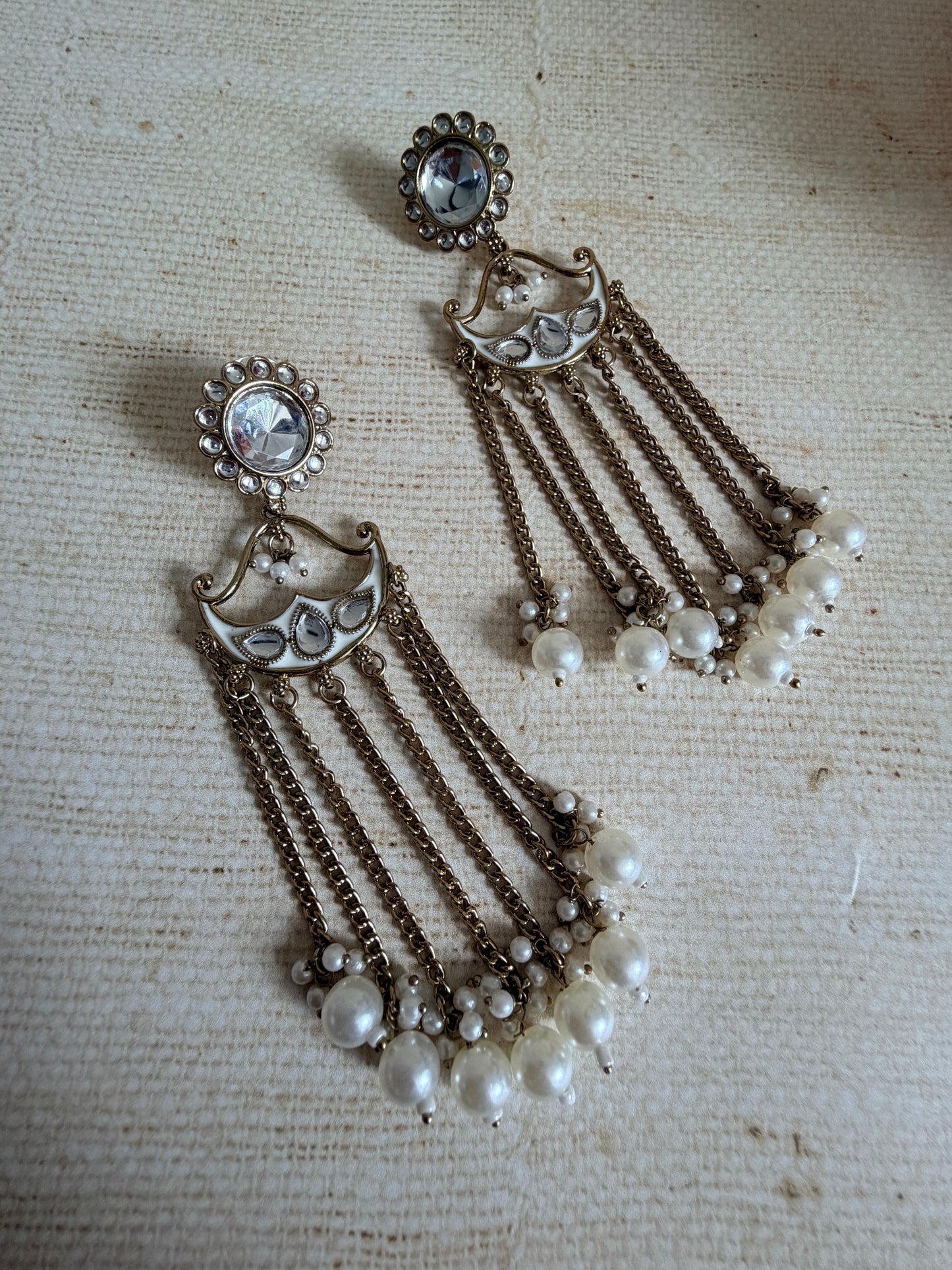 Pair of ornate earrings with chains and pearls on a textured surface