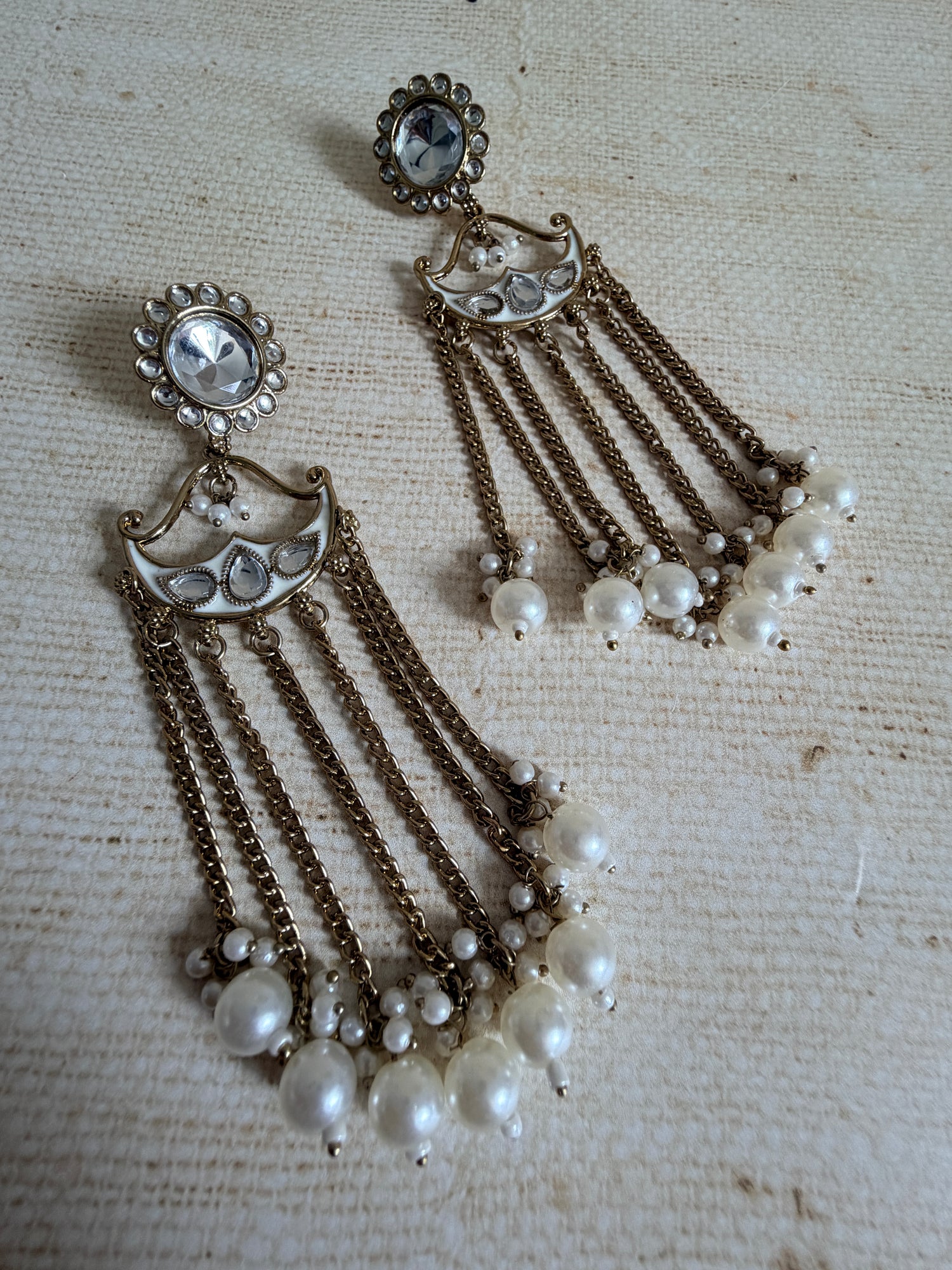 Vintage-style jewelry set with pearl-like beads and metallic chains on a textured beige background
