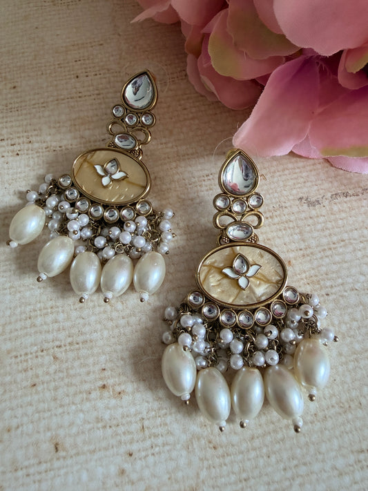 Pair of ornate earrings with pearls on a textured surface with pink flowers.