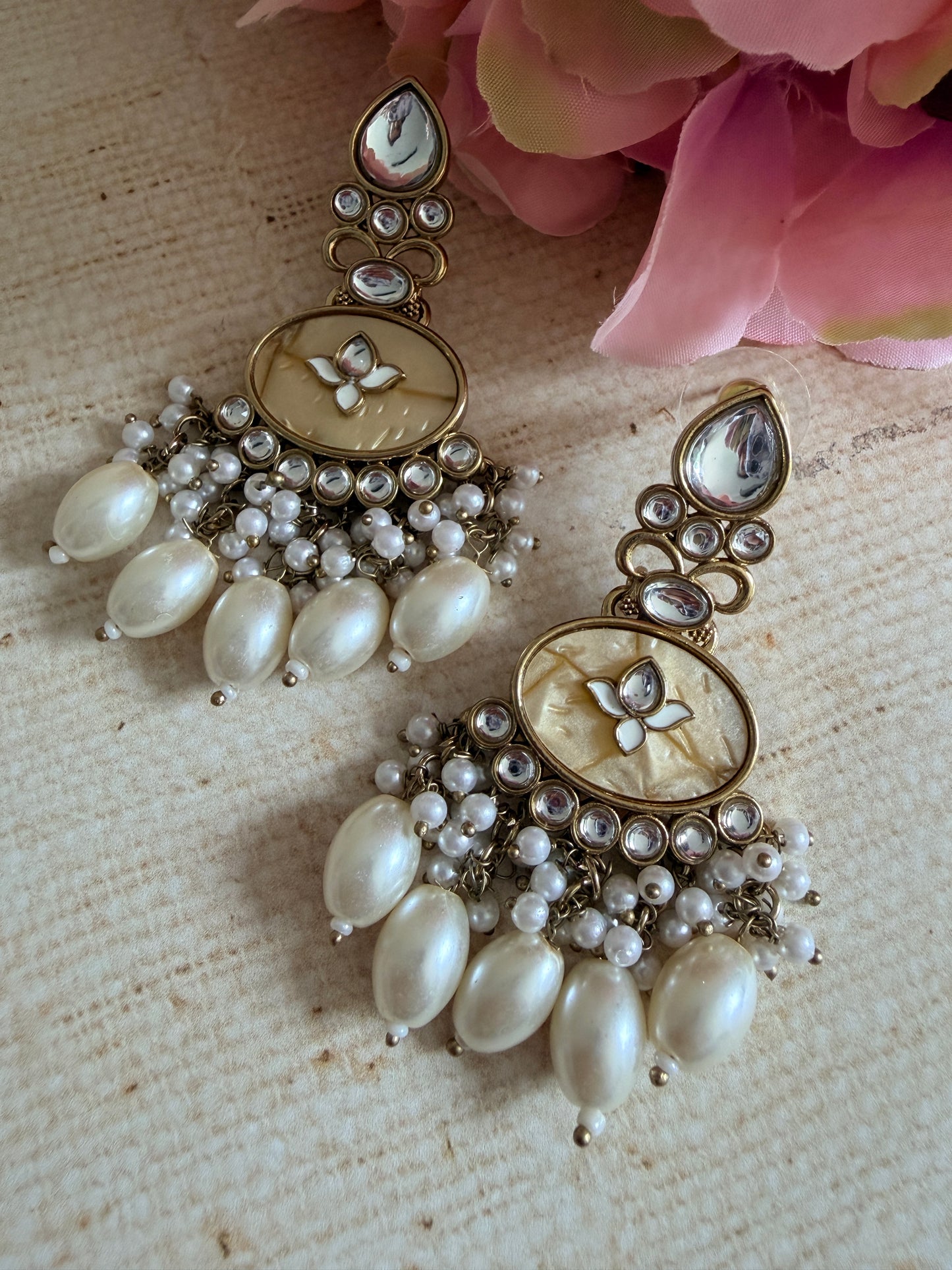 Pair of ornate earrings with pearls on a textured surface with pink flowers.