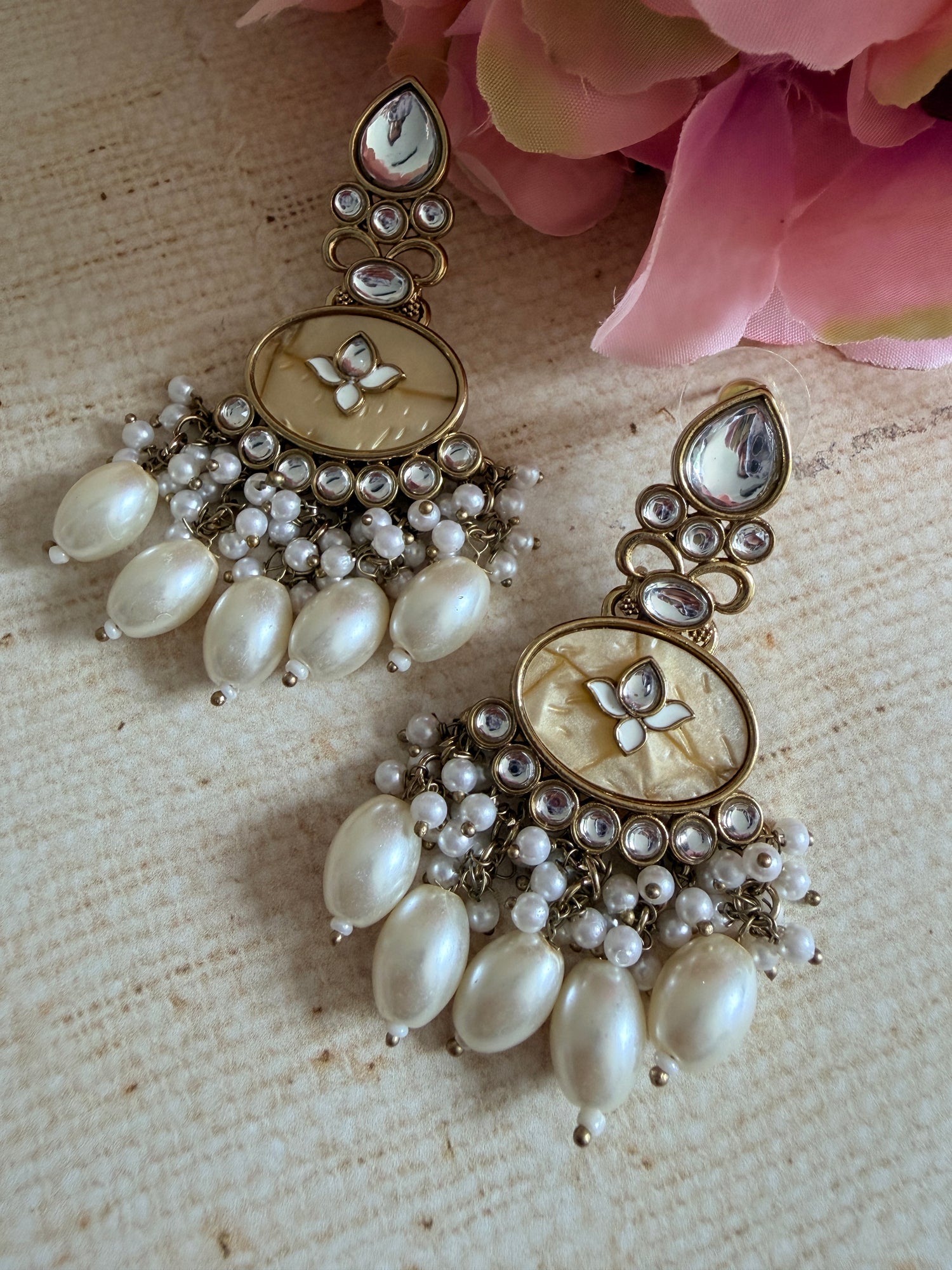 Pair of ornate earrings with pearls on a textured surface with pink flowers.