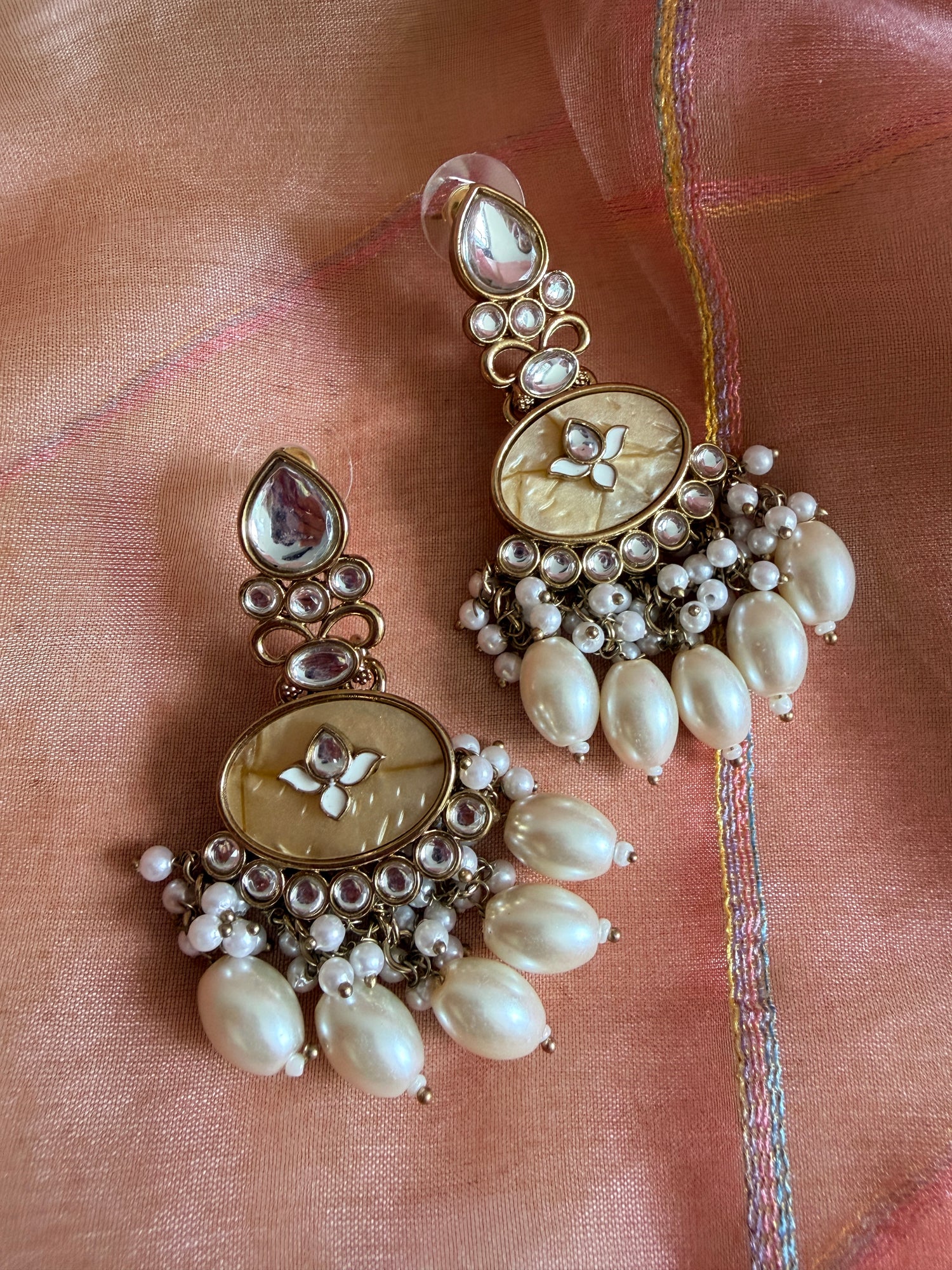 Pair of ornate earrings with pearls on a pink fabric background