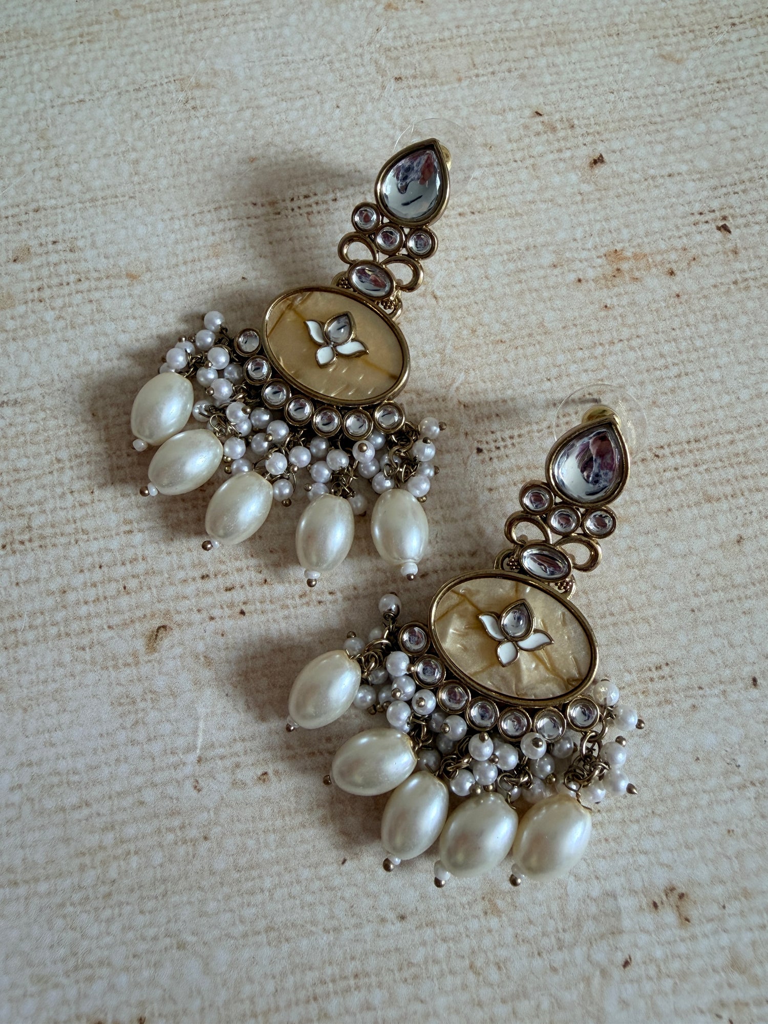 Pair of ornate earrings with pearls and gemstones on a textured beige surface