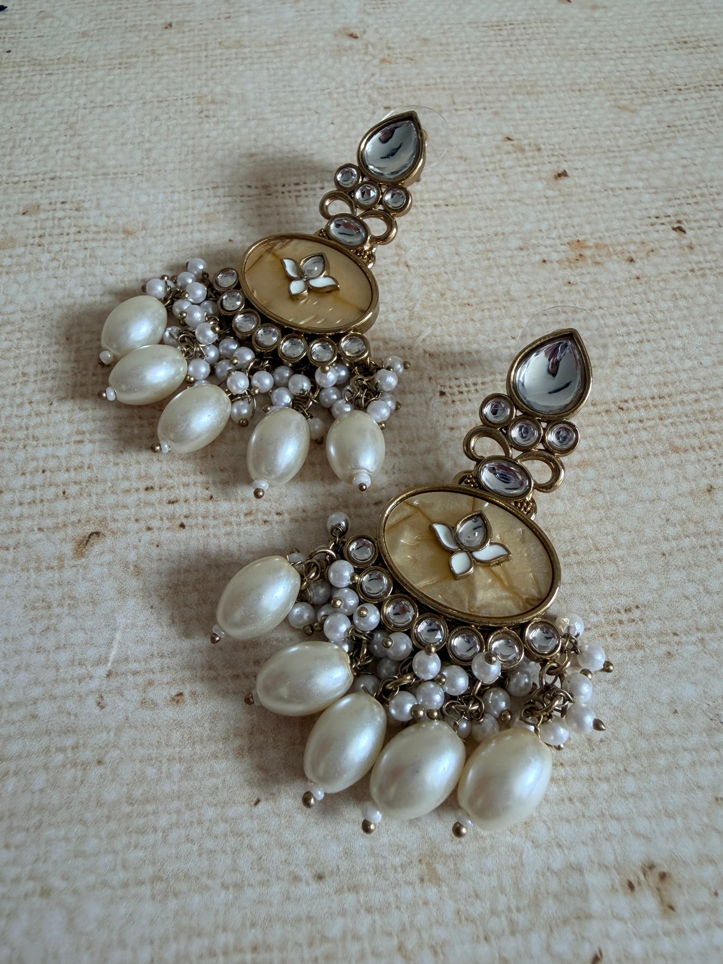 Pair of pearl and gemstone earrings on a textured beige background