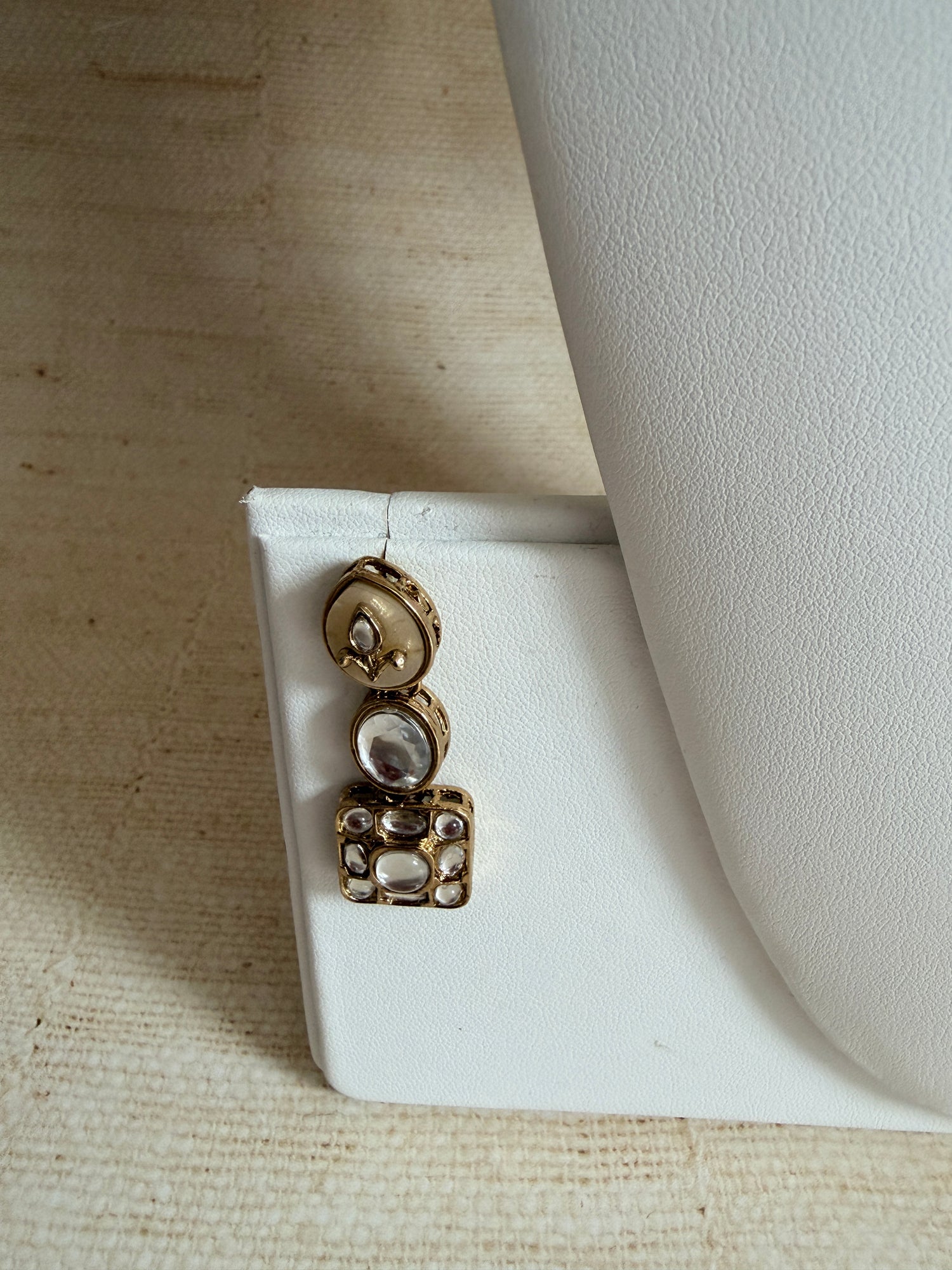 Gold earrings with gemstones on a white stand against a beige background