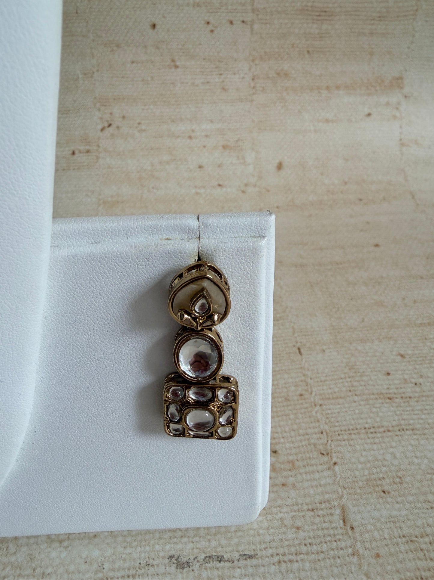 Gold earrings on a white stand against a beige textured background