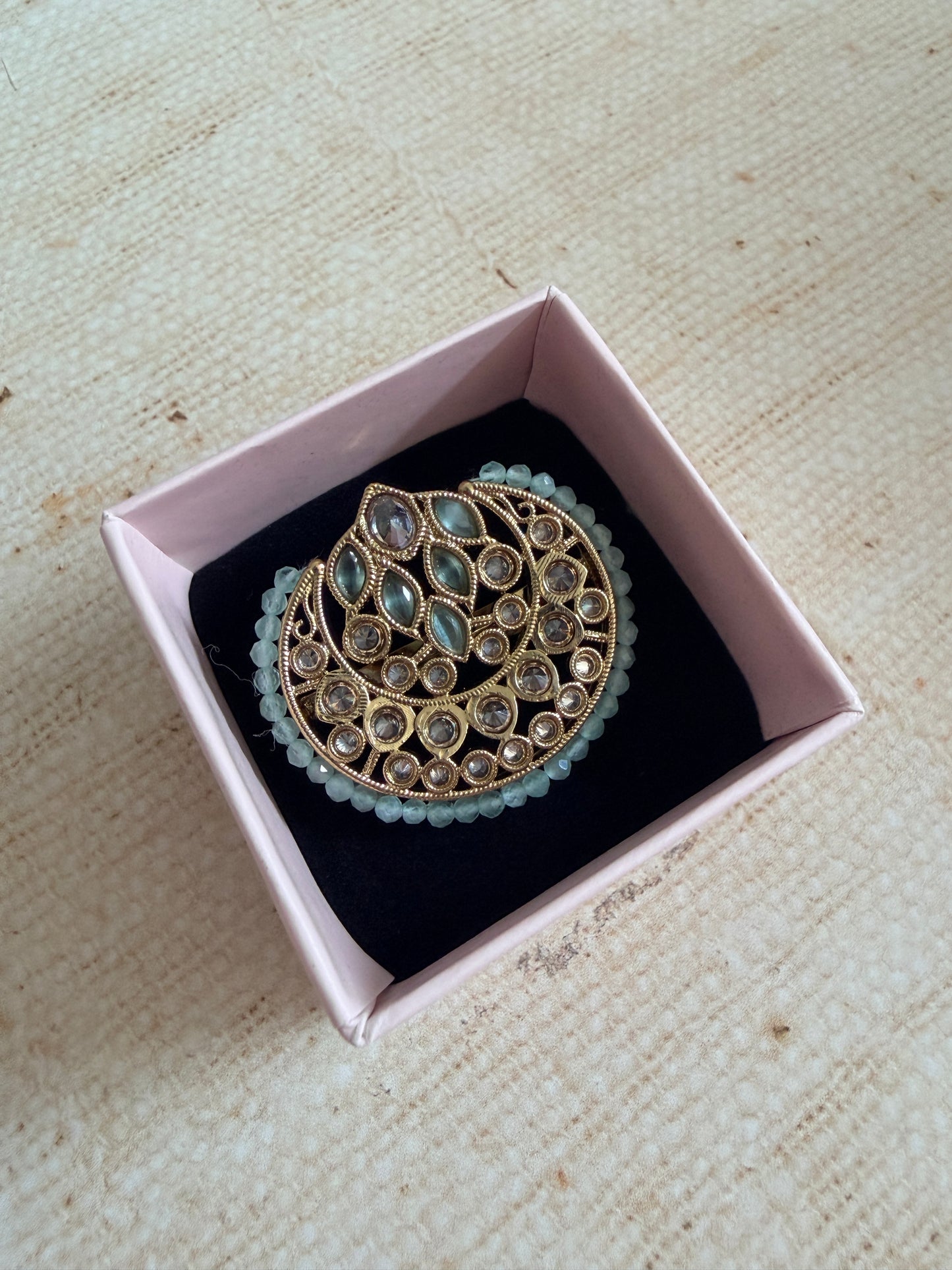 Decorative brooch in a pink box on a textured beige surface