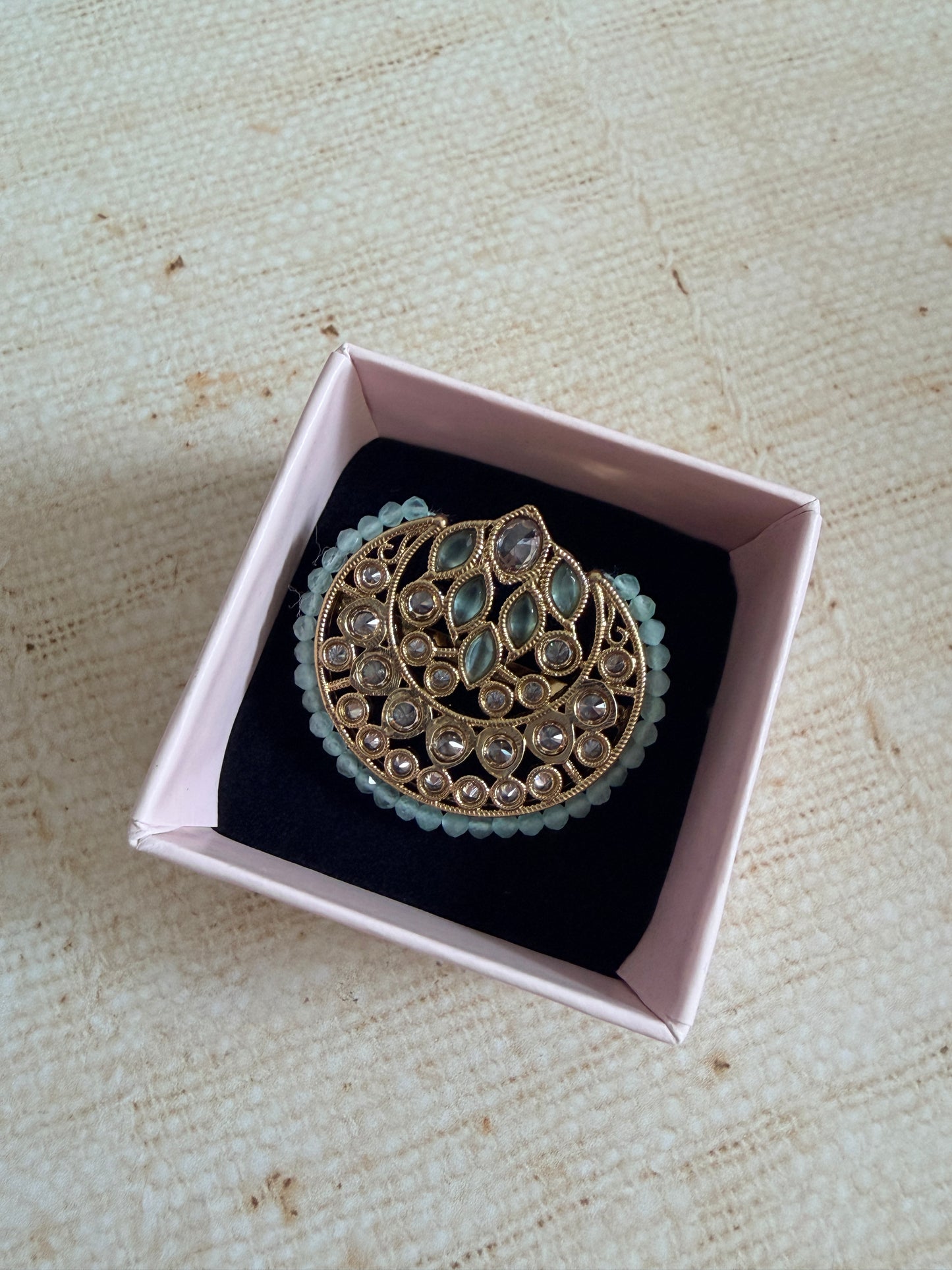 Decorative brooch in a pink box on a textured beige surface