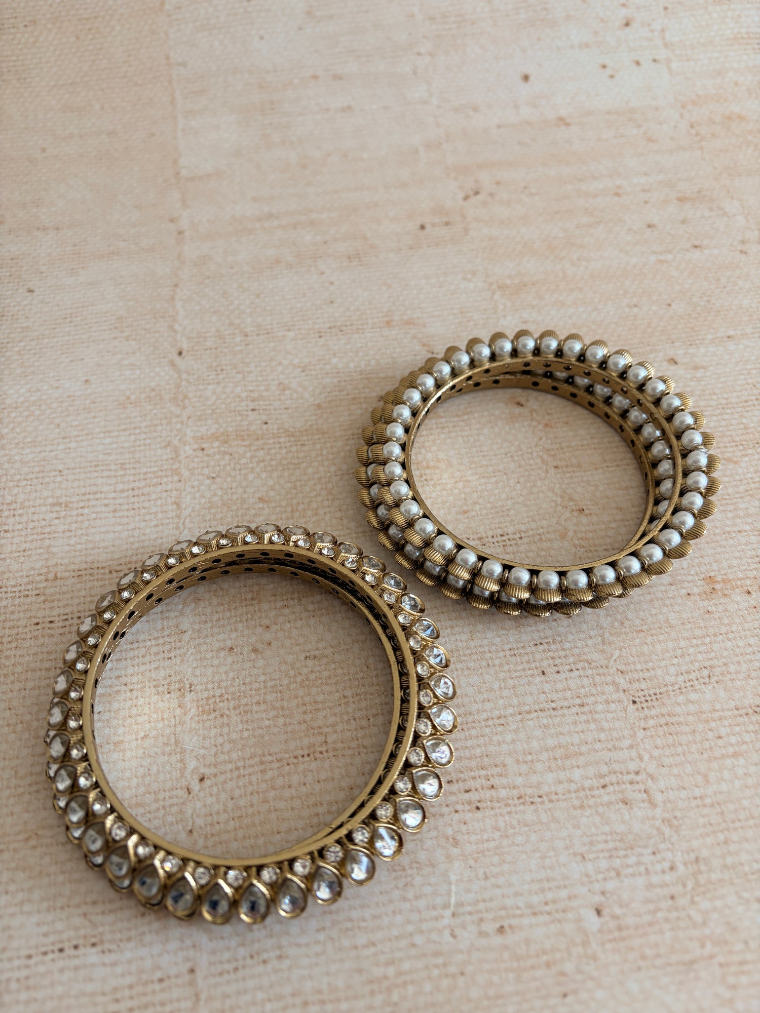 Two metallic bangles with beaded detailing on a textured beige background