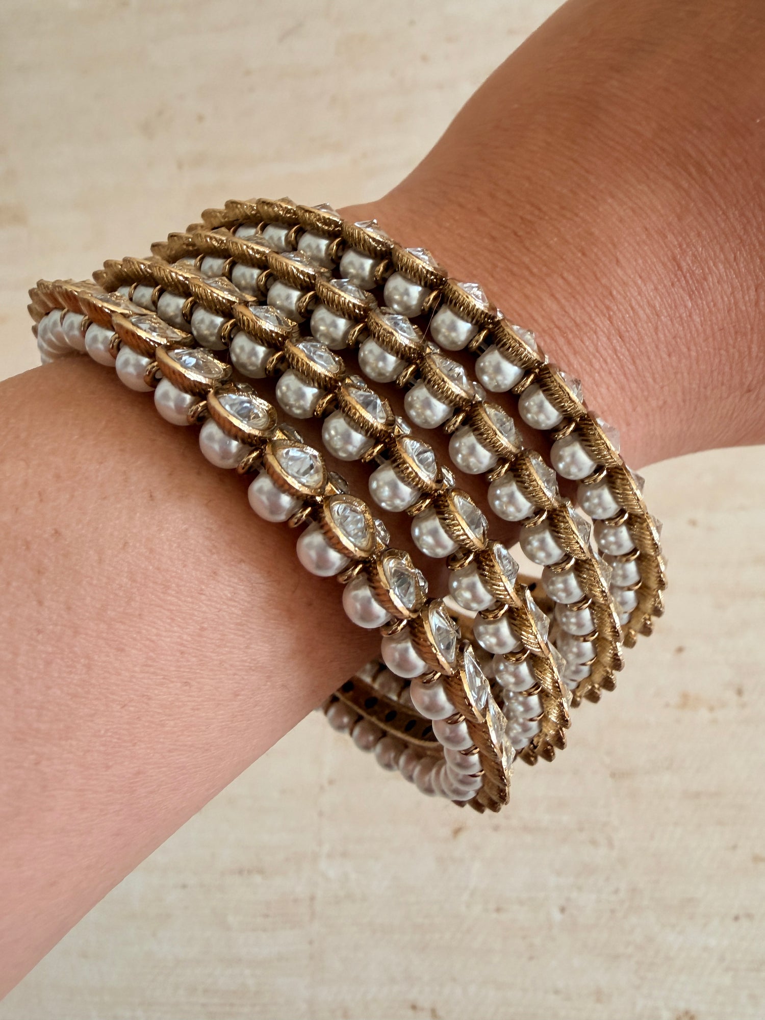 Multiple pearl and gold bracelets on a wrist against a neutral background