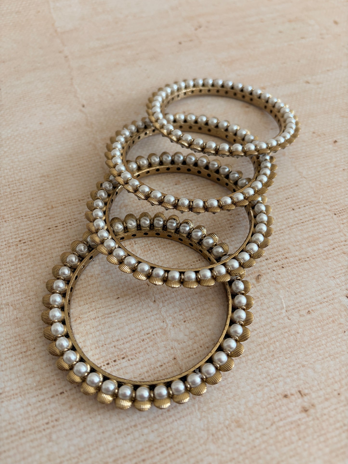 Set of pearl and gold bracelets on a beige fabric background