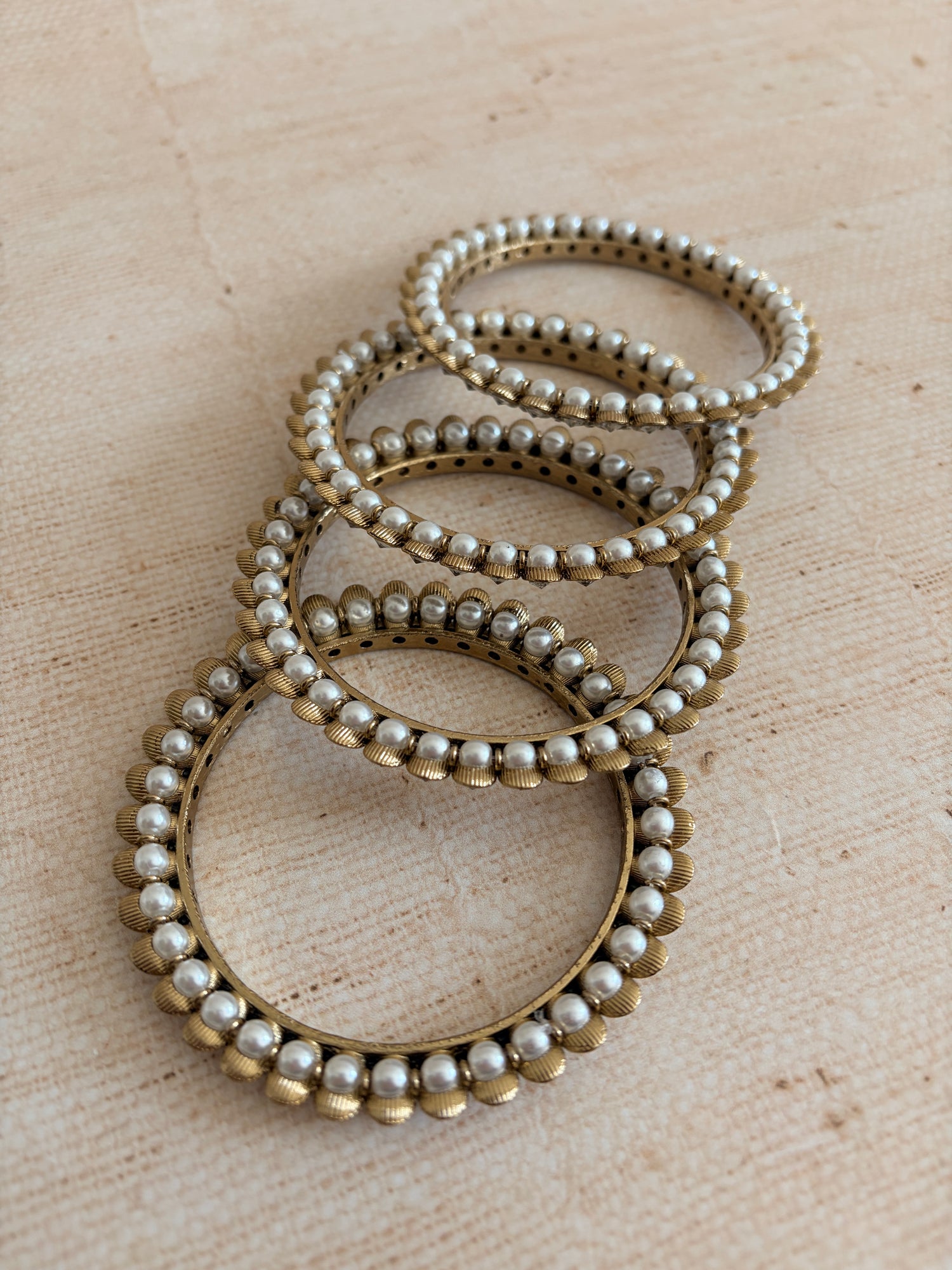 Set of pearl and gold bracelets on a beige fabric background