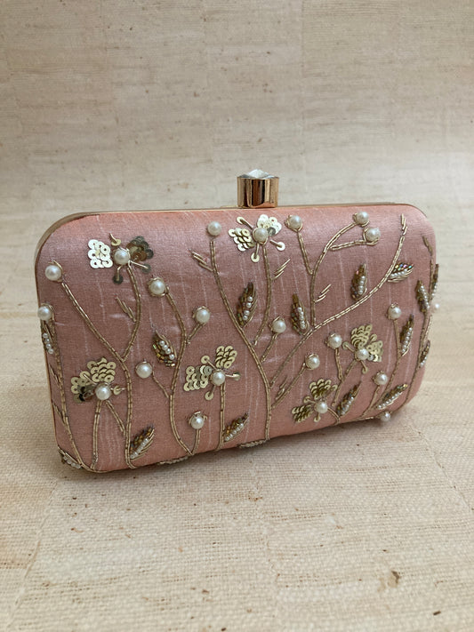 A light pink rectangular silk clutch with zardozi work, sequins, and pearl embellishments, featuring a floral pattern.