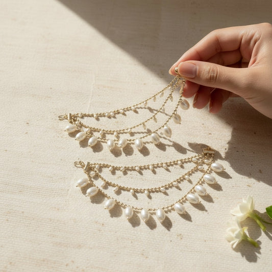 Hand holding a delicate gold and pearl necklace on a beige surface with a soft shadow.